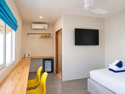 Long wooden desk, yellow chairs, television and small fridge in a beach bungalow