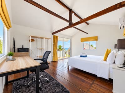 Beach house interior with a double bed, long desk and exposed roof beams