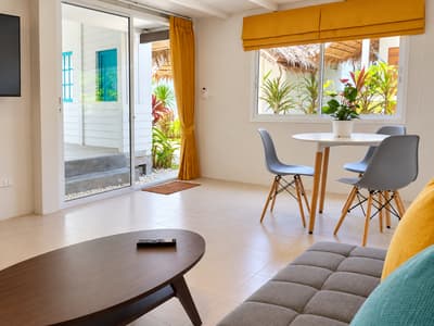 Beach house living room with a grey sofa, coffee table and dining table beside sliding glass doors