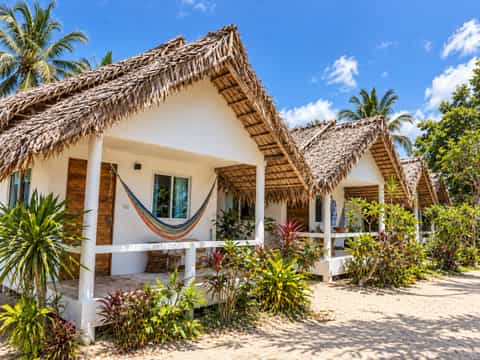 Thatched beach bungalows with terraces and hammocks beneath palm trees