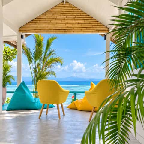Yellow chairs and colourful beanbags on a shaded terrace overlooking the turquoise sea