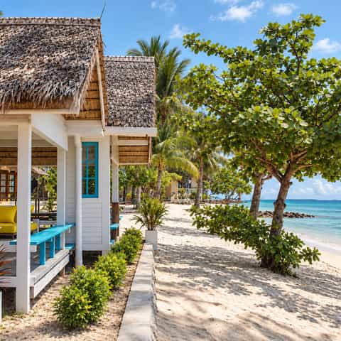 Thatched white bungalows beside a sandy beach, tropical trees and turquoise sea