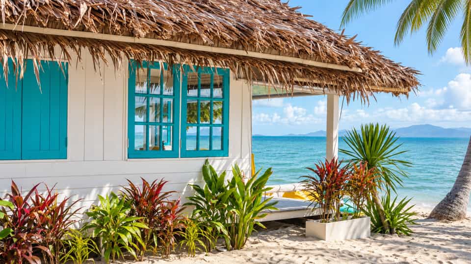 White thatched bungalow with turquoise windows beside the beach and sea
