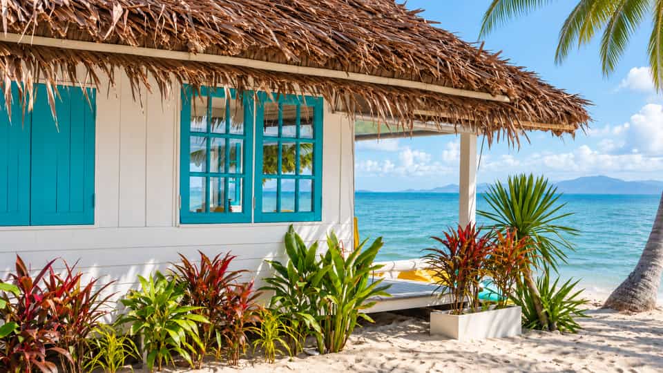 White thatched bungalow with turquoise windows beside the beach and sea